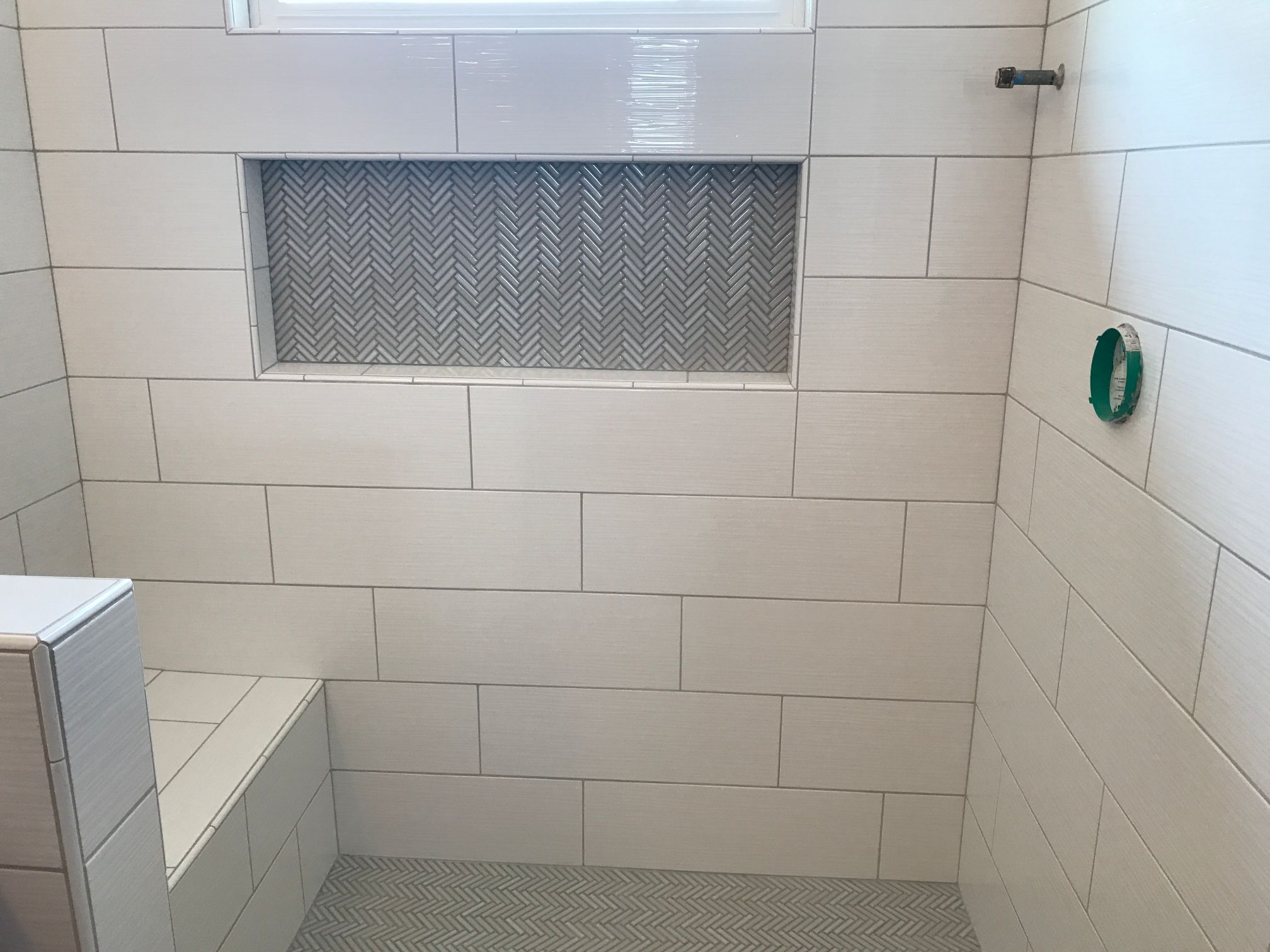 Herringbone pattern on custom tile shower shelf and floor with a bench seat.