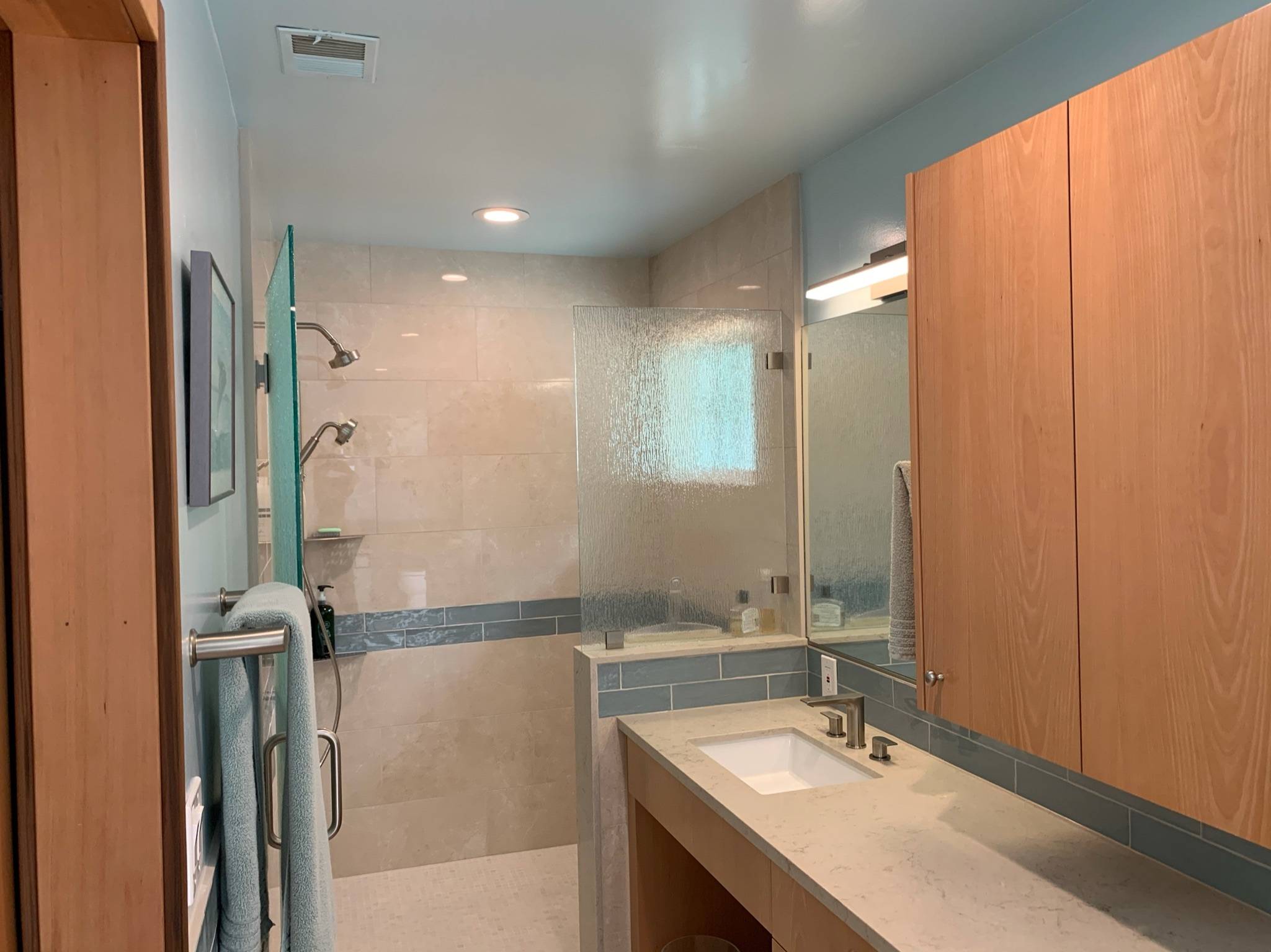 This curbless shower has mosaic floor tile. The wall tiles have a marble look with a reflective, polished finish, and there is a decorative strip.