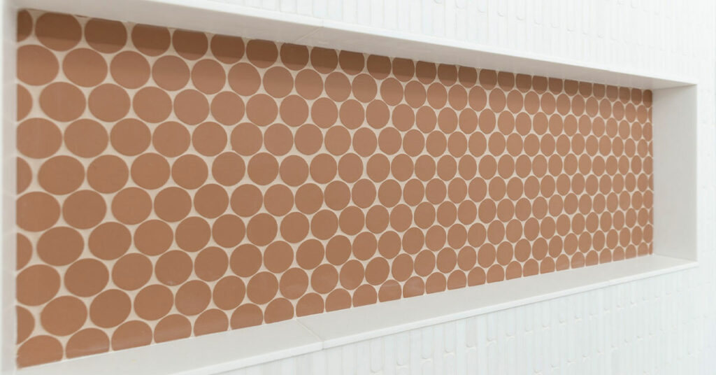 Shower niche with round, earth-tone mosaic tiles.