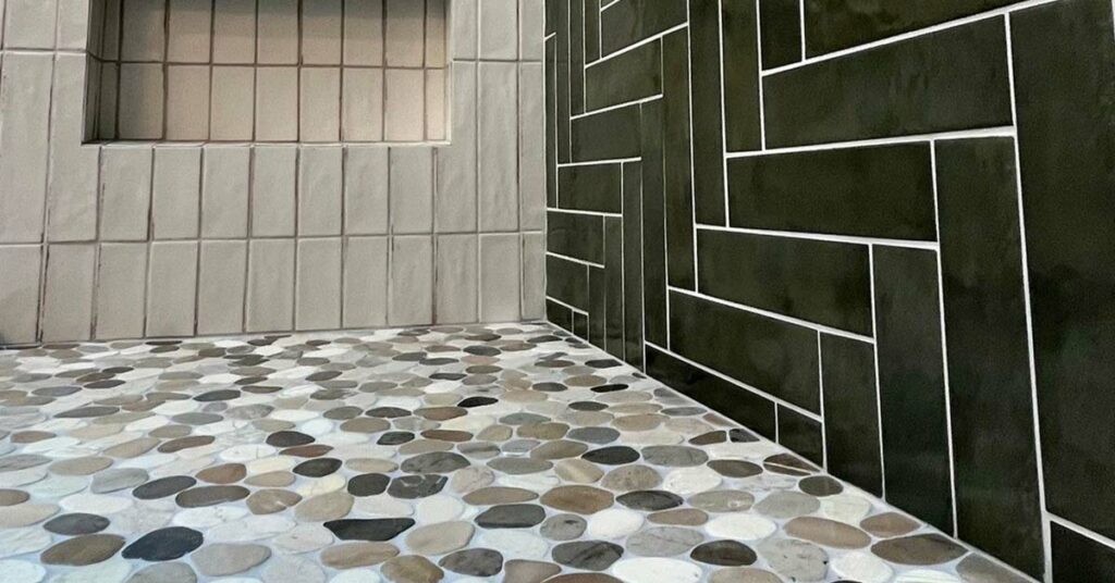 Ceramic tile shower walls and niche and natural stone tile pebble shower floor.
