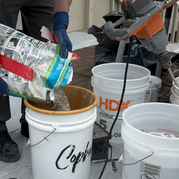 Tile installers use many different types of materials and products. In this image, a tile installer is pouring a bag of thinset into a bucket. Nearby, there are tools for mixing the thinset.